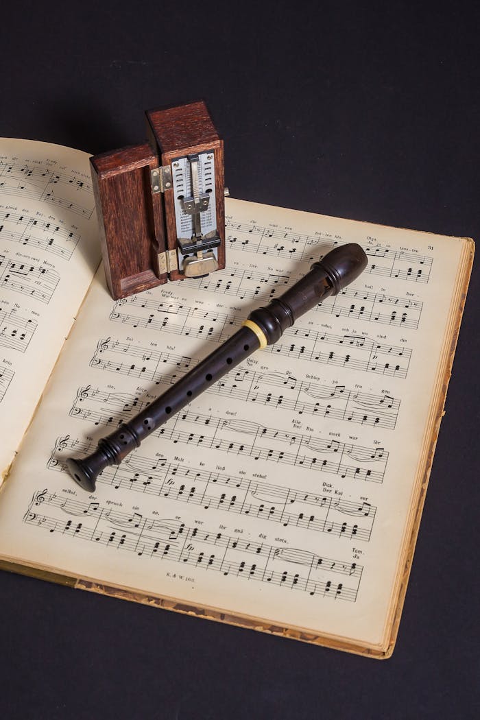A wooden flute resting on a music sheet with a vintage metronome, showcasing a classic musical theme.