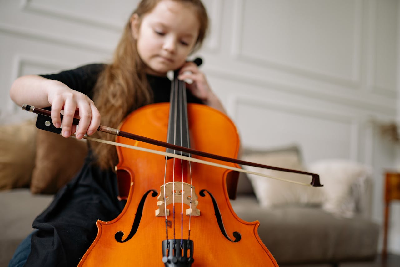 Young girl enjoying classical music by playing the cello indoors.